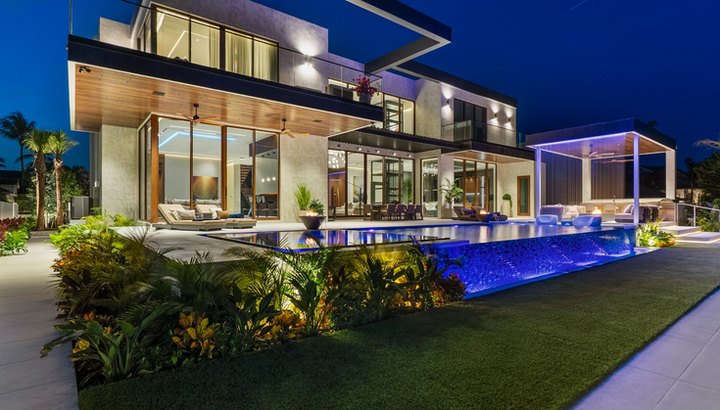 New-construction waterfront estate at dusk with illuminated infinity-edge pool